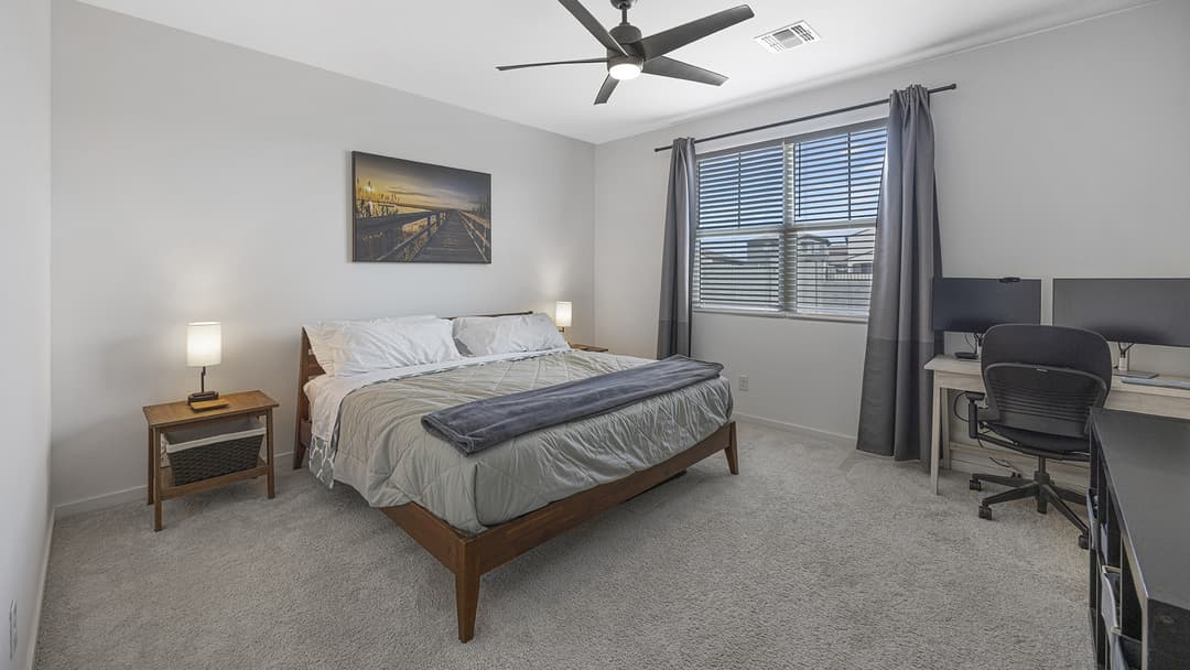 A serene primary bedroom featuring a large bed and an integrated professional workspace with two monitors